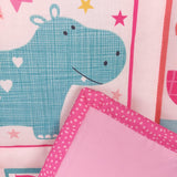 a smiling blue hippo with white hearts on its side surrounded by stars. The binding of pink spots is folded onto the quilt
