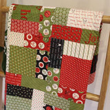 a Christmas quilt of different-sized squares and rectangles in greens, red, white, and black. There are numbers counting down the days to Christmas 