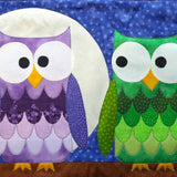 two owls sitting next to each other on a brown branch. One owl's feathers are different shades of purple and the other is green. They are sitting in front of a giant moon.