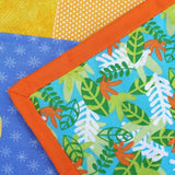 A close up of the quilt backing fabric which is jungle leaves in different shades of green and an orange binding of the quilt edges.