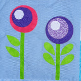 A blue spotted fabric background with 2 flowers in purples and pinks with bright green stalks and leaves